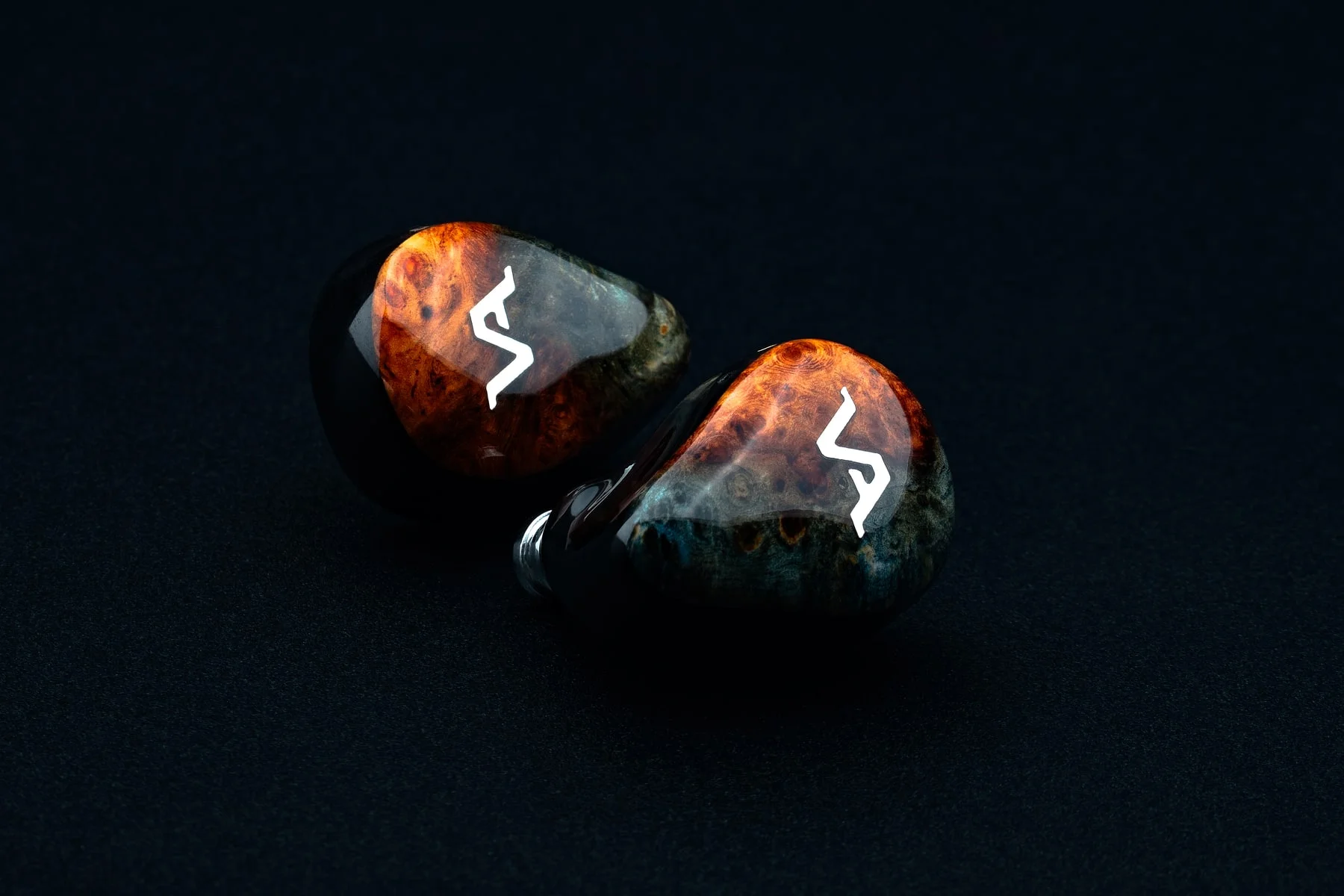 A pair finished in fire-and-teal stabilised burl, angled on a matte black backdrop