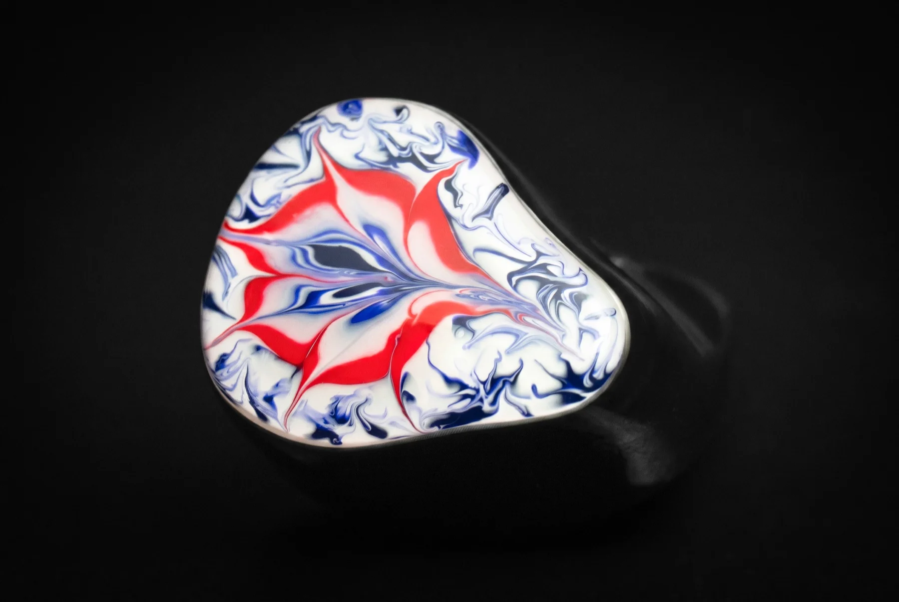 A single earpiece from above, its faceplate marbled in red, white and blue over a black shell